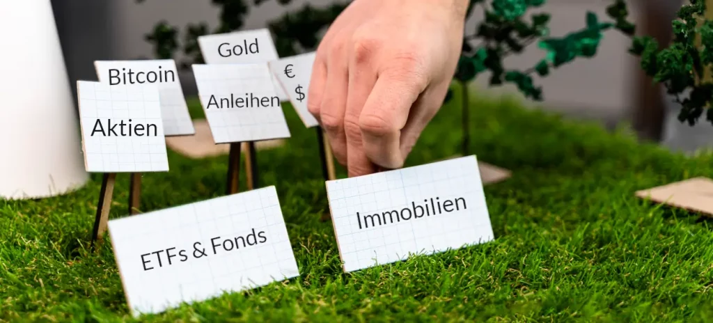 Ein Mann positioniert Schilder mit Geldanlagen wie Aktien, Immobilien und Anleihen auf einer Miniatur-Wiese.