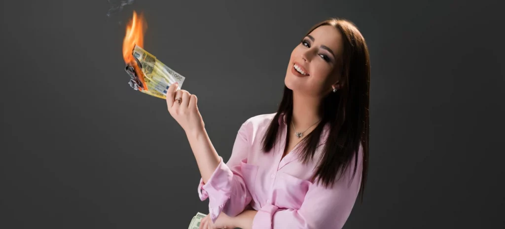 Frau hält lachend brennendes Geld in der Hand vor einem dunklen Hintergrund.