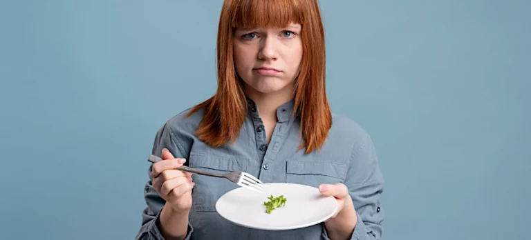 Eine junge Frau sitzt mit enttäuschtem Gesichtsausdruck vor einem fast leeren Teller – eine Metapher für die schleichende Geldentwertung, bei der man für sein Geld immer weniger bekommt.