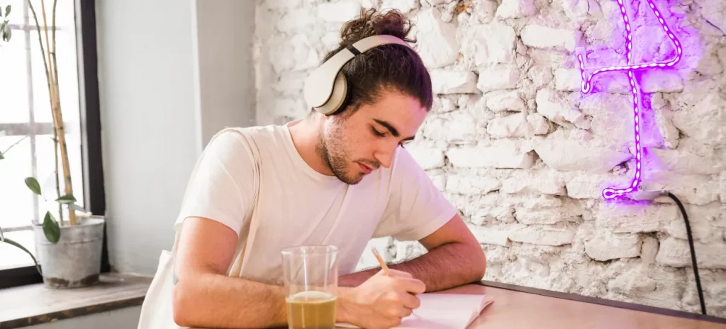 Ein junger Mann mit Kopfhörern schreibt seine Zielsetzung konzentriert in ein Notizbuch.