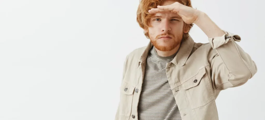 Ein junger Mann mit ernstem Blick hält sich die Hand über die Augen, um in die Ferne zu sehen – Symbol für aktives Erkennen von Chancen trotz Zukunftsangst.