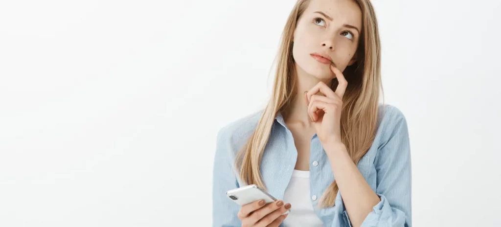 Nachdenkliche junge Frau mit Smartphone in der Hand blickt zur Seite und überlegt, ob es sich um ein Schneeballsystem handelt oder nicht.
