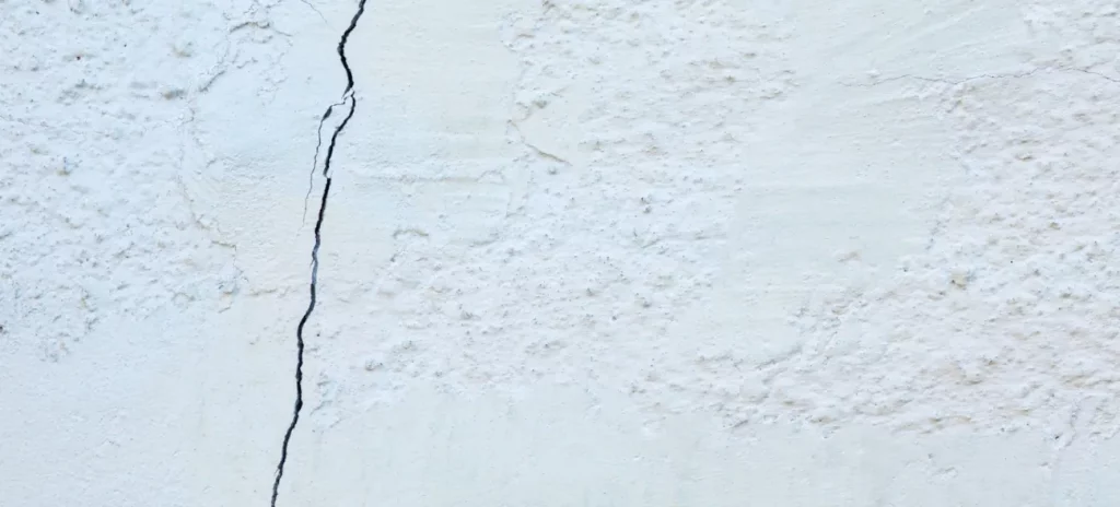 Ein feiner Riss zieht sich durch eine weiße Wand. Glaubenssätze auflösen: Er steht symbolisch für die ersten sichtbaren Folgen negativer Gedankenmuster, die zu inneren Spannungen führen.