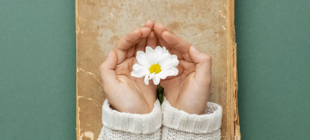 Eine Frau umschließt mit den Händen schützend eine weiße Blume. Sie symbolisiert den gefundenen Sinn des Lebens und die damit verbundene Erfüllung und Zufriedenheit.